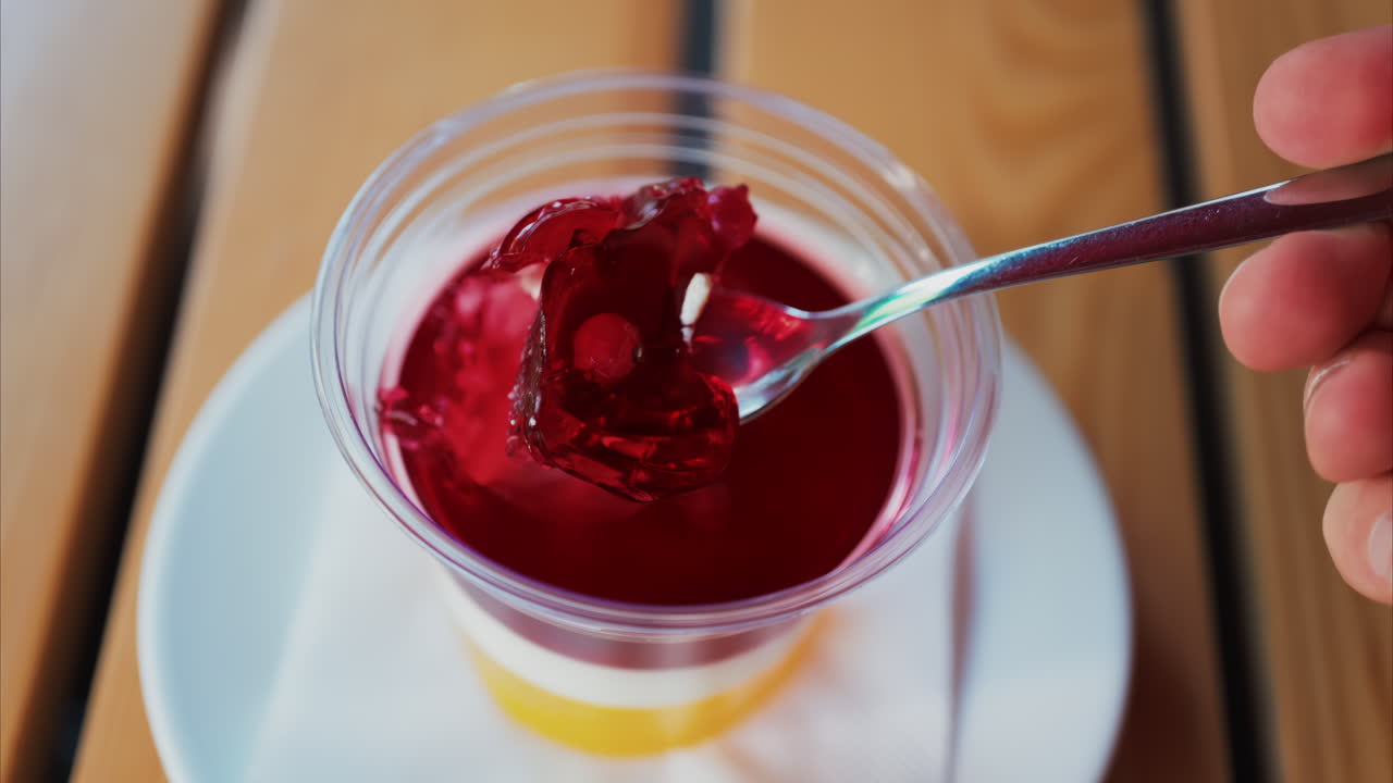 Close up of a bright layered jelly dessert in a clear cup on a wooden table