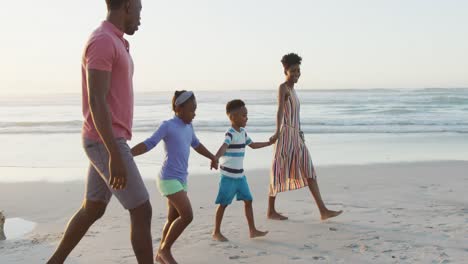 happy african american couple walking with daughter and son on sunny beach