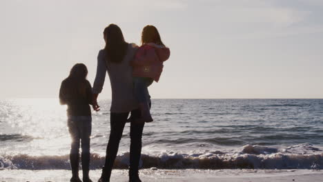 rear view of mother with daughters looking out to sea silhouetted against sun