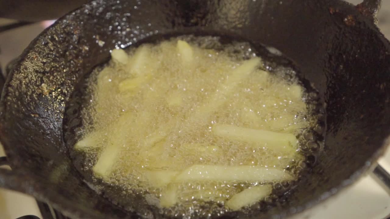 Homemade French fries deep frying in vegetable oil in hot wok, closeup