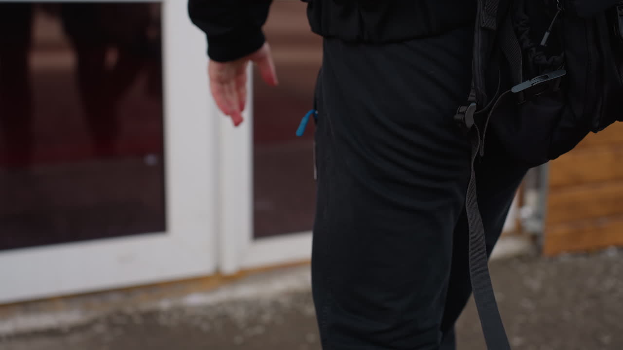 Close up of young man s hand resting near leg while walking into a door , dressed in dark clothing, casual fashion detail shot, sunlight highlighting skin tone against black fabric background