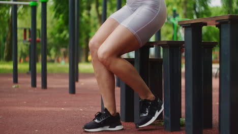 una mujer joven en un parque realiza ejercicios caminando en un banco con ropa deportiva en el verano.