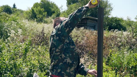 mature man measures height of fence metal pole with tape