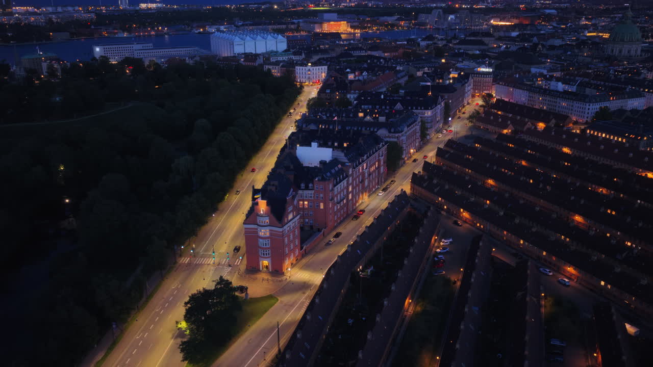 Aerial drone view of the triangular building lit up at night along Oster Voldgade, Copenhagen, Denmark