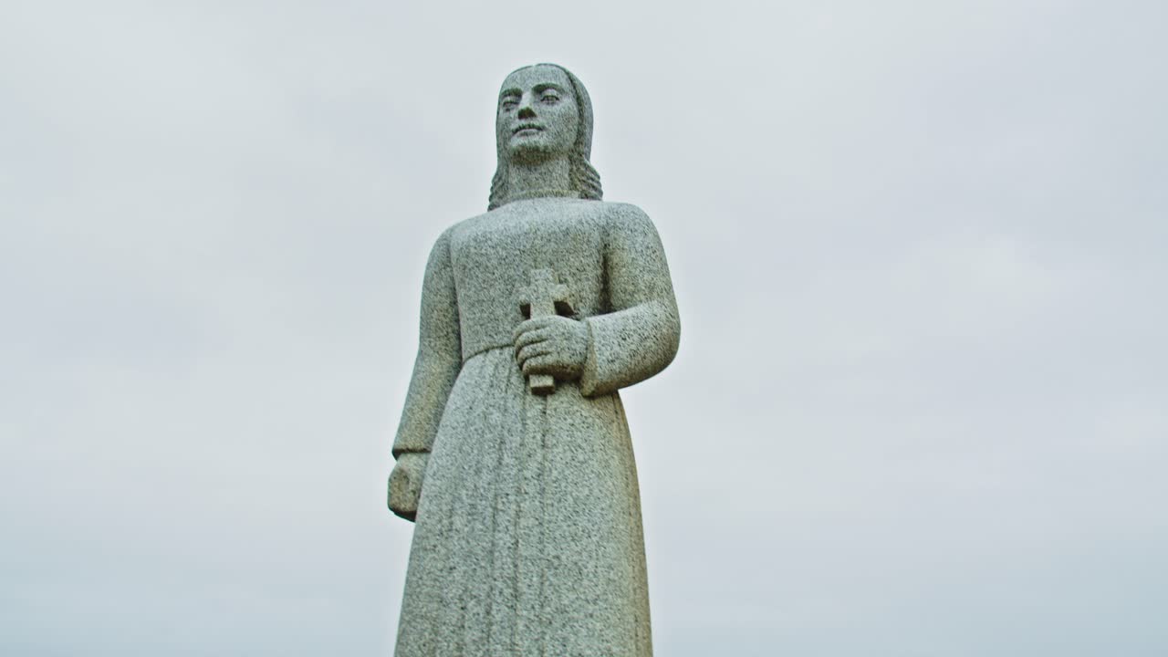 Affascinante ripresa a mano della statua di Landsýn di una donna che tiene un crocifisso presso la chiesa di Strandarkirkja in Islanda in una giornata nuvolosa.