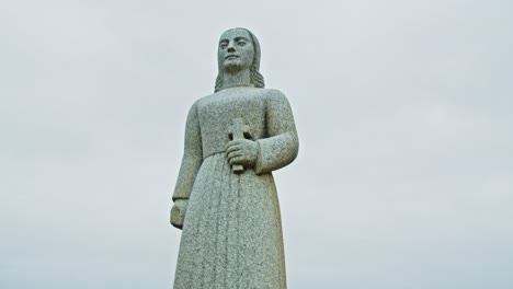 Captivating-handheld-view-of-Landsýn-statue-of-a-woman-holding-a-crucifix-at-Strandarkirkja-church-in-Iceland-on-a-overcast-day