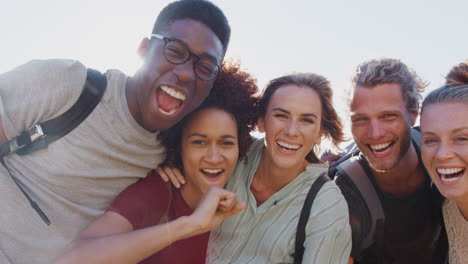 portrait of young friends hiking celebrating reaching the peak of coastal cliff against flaring sun