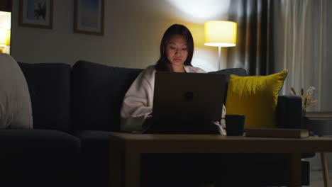 woman spending evening at home sitting on sofa with laptop computer looking at social media streaming or scrolling online 5