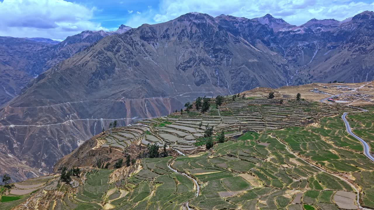 Um drone em movimento reverso se afasta da borda do cânion para revelar terras agrícolas em socalcos, enquanto toda a altura e o poder da paisagem montanhosa do cânion de Colca surge, incluindo a abertura dramática do cânion