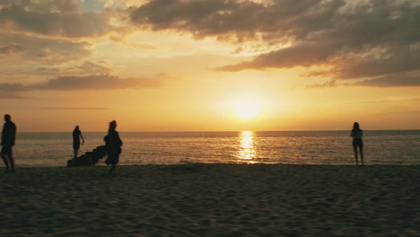 disparo de dron volador lateral bajo de personas caminando en la playa durante la puesta de sol