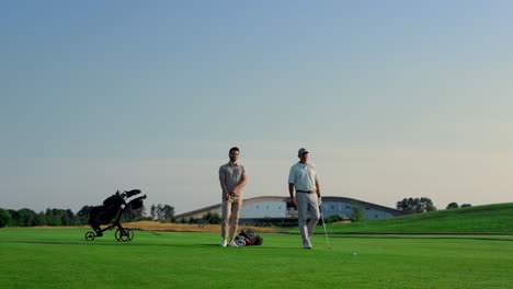 Two-golf-players-talk-game-preparation-on-green-grass-field-course-outdoors.