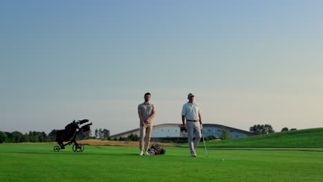 two golf players talk game preparation on green grass field course outdoors.