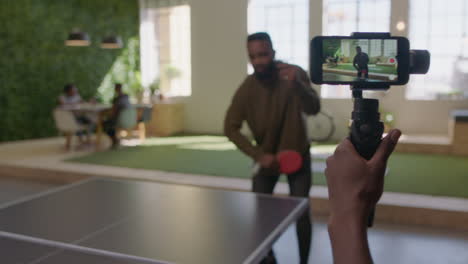 jóvenes hombres de negocios negros jugando al ping pong en la oficina disfrutando de la diversión competitiva colega usando el teléfono inteligente compartiendo el juego en las redes sociales tomando video