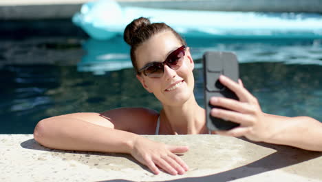 Una-Adolescente-Con-Gafas-De-Sol-Se-Toma-Un-Selfie-Junto-A-La-Piscina-Y-Frunce-Los-Labios-Para-La-Cámara.