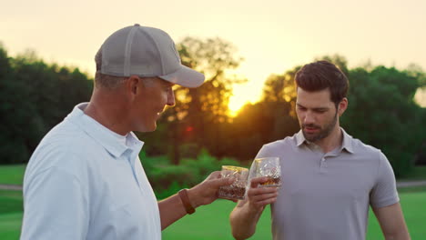 Two-golfers-chatting-together-at-green-course.-Golf-team-drink-whiskey-outside.