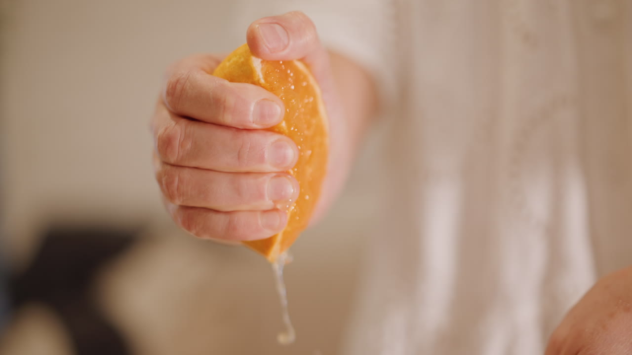 Un agarre firme extrae un vibrante líquido cítrico. El primer plano revela pulpa y gotas a medida que el jugo fluye. El movimiento táctil de exprimir libera jugo de cítricos fresco, rico en sabor y vitalidad.