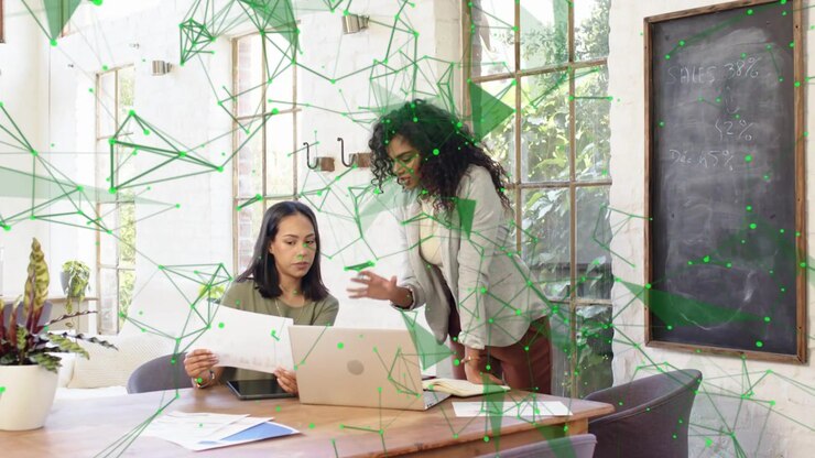 Mentore che si china per guidare un collega tramite laptop per un controllo aziendale, con una sovrapposizione verde che si anima sulla scena.