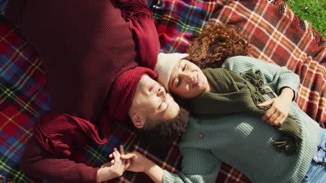 video of biracial couple warmly dressed lying on blanket spending time in the garden