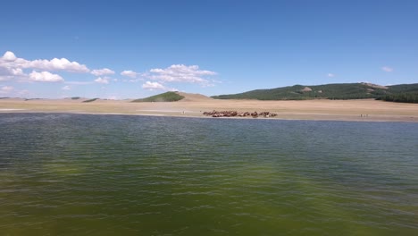 Zoom-in-from-lake-in-mongolia-to-herd-of-horses-walking-along-the-water.-Aerial