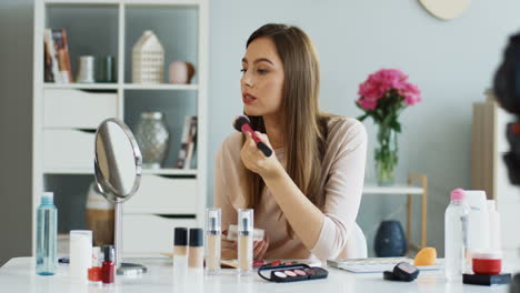 pretty beauty blogger recording a makeup tutorial video and teaching how to apply blush on cheeks