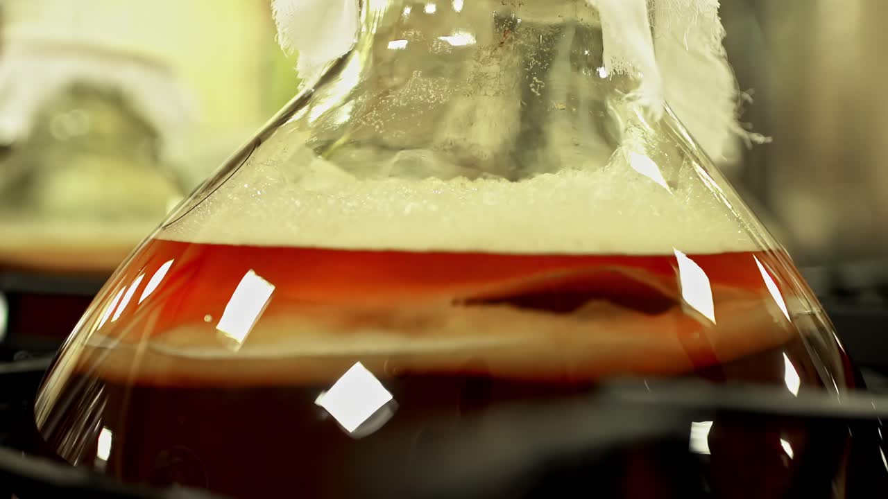 Amber liquid in a large glass vase reflects bright square lights, creating visual glow