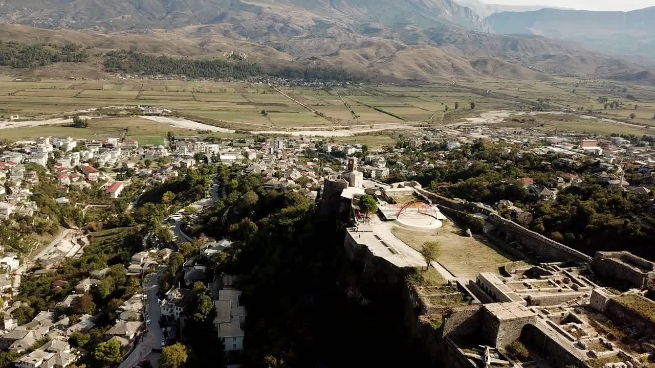 vista desde un avión no tripulado del castillo de gjirokaster, albania, balcanes, europa panning shot de la torre del campanario con montañas en el fondo