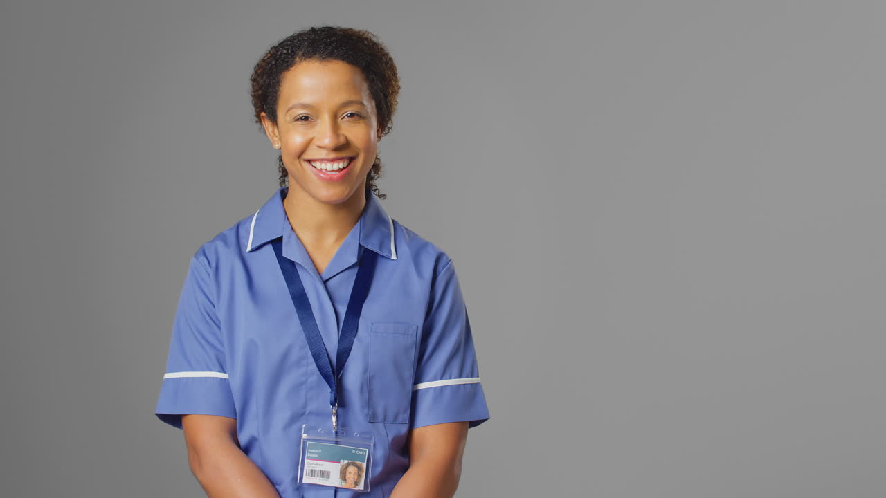 retrato de estudio de una enfermera vestida de uniforme sonriendo a la cámara contra un fondo gris