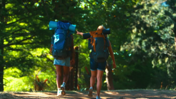 Dos amigas con mochilas chocando las cinco mientras inician sus vacaciones de senderismo.