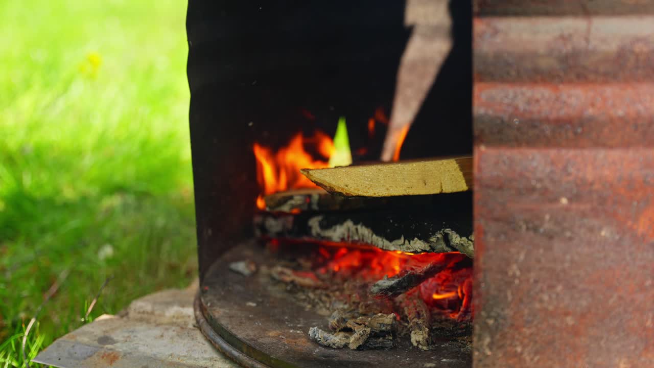 Flames rise around kettle as wood burns for rustic outdoor soup preparation in daylight, slow motion detailed establishing of wood catching fire