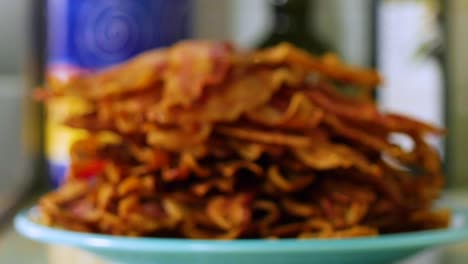 pile of crispy bacon strips stacked on plate on counter, close up focus pull