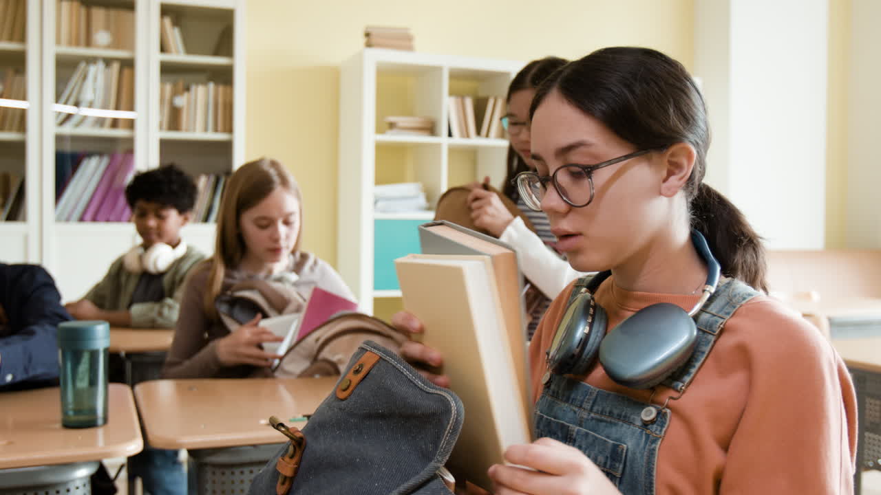 Students in a classroom putting books and supplies into their backpacks