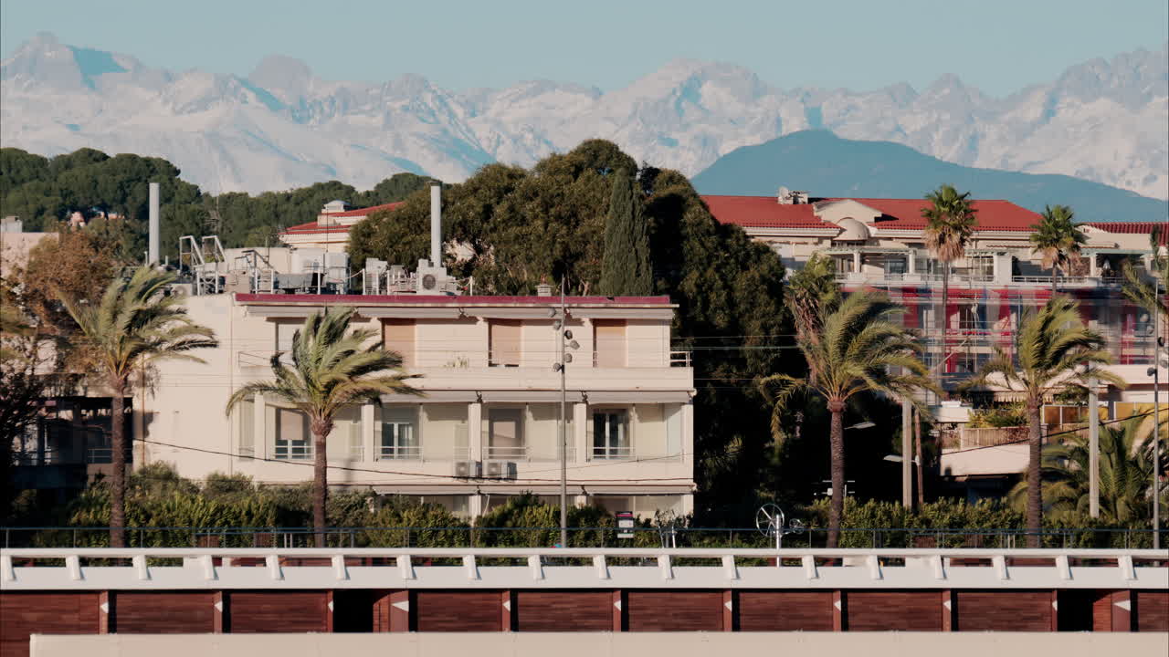 Buildings and palm trees on the shore with a view of the mountains in the background in Antibes, France