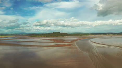 Aerial-landscape-of-a-costal-bay-at-low-tide,-with-the-wet-sand-shimmering-in-the-sunlight