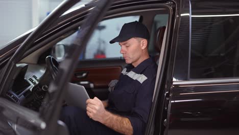 car mechanic working on laptop in auto repair service inside the car