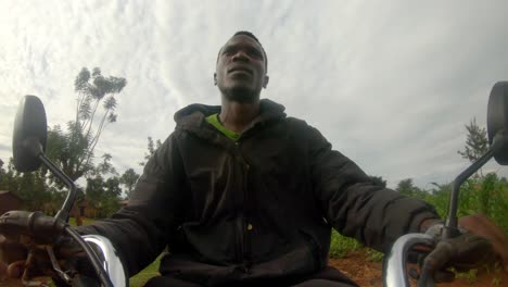 a action shot of an african mans face while steering a motor bikes handle bars rides through a african village