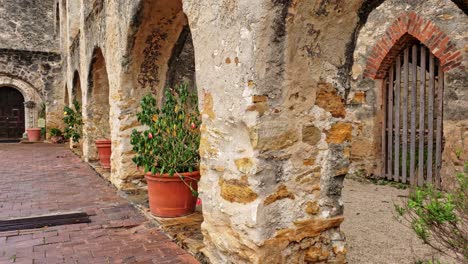 looking-through-old-mission-arches,-plant-pots-trees-and-colorful-old-fort-compound