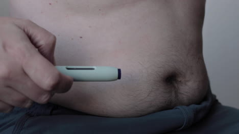 close up of self applying of medicine through a medical needle pen injecting the substance in a fatty area of the abdomen leaving a drop of blood as a mark