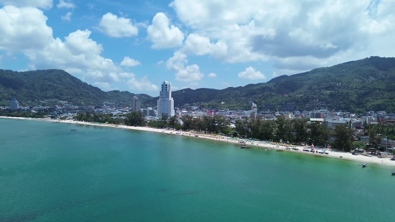 Pemandangan udara Patong yang menunjukkan perpaduan garis pantai dan bangunan hotel padat dengan lingkungan tropis serta air laut biru kehijauan yang jernih di Phuket, Thailand, destinasi wisata yang semarak.