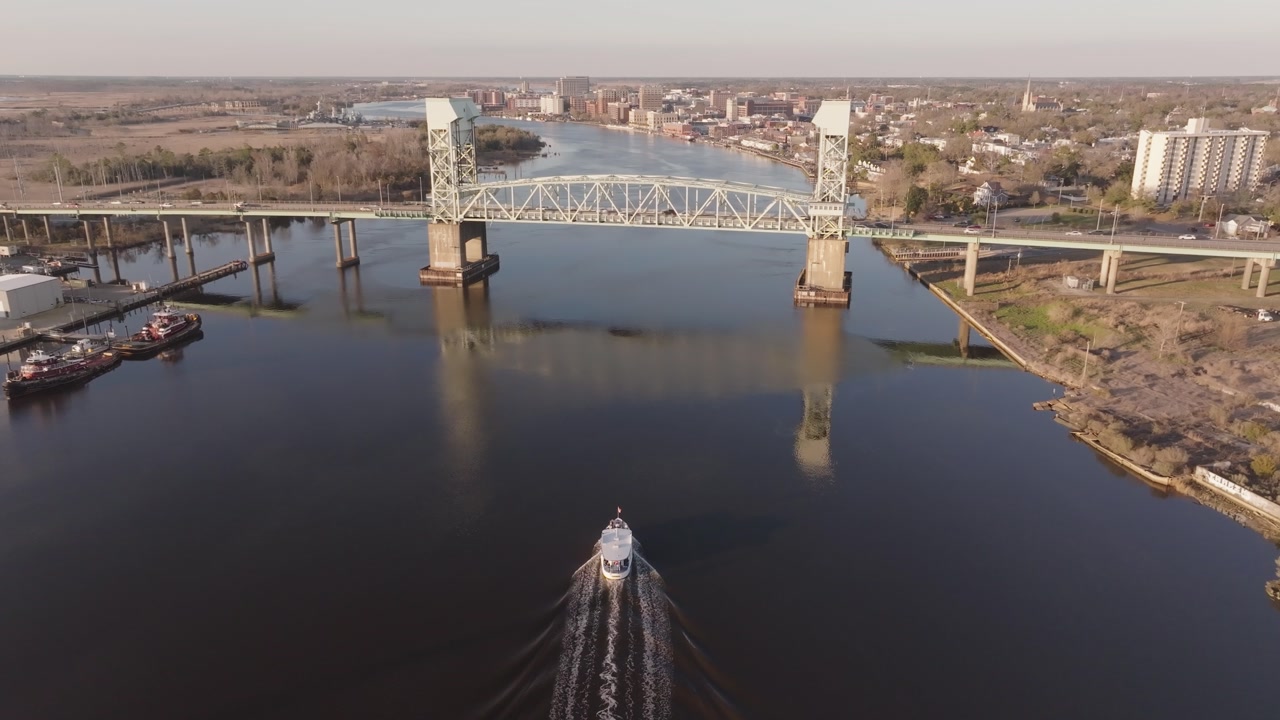 A 4k drone shot following a boat as it enters a coastal town with an iconic bridge in North Carolina