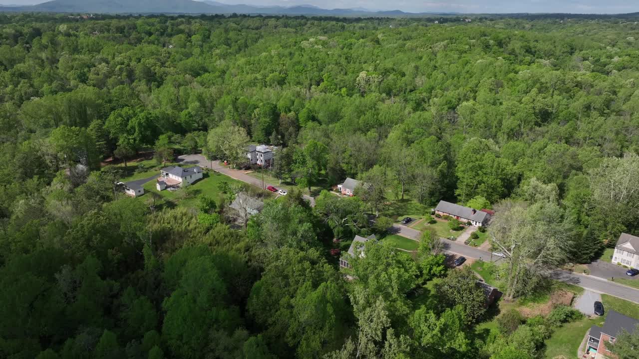 One family homes between green forest trees during sunny day in spring. American suburb neighborhood of Lynchburg, Virginia. Aerial approaching wide shot.