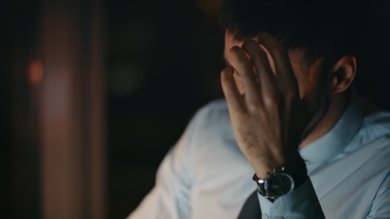 Empresário desesperado sentado no escritório, preocupado e sentindo estresse à noite, em close-up.