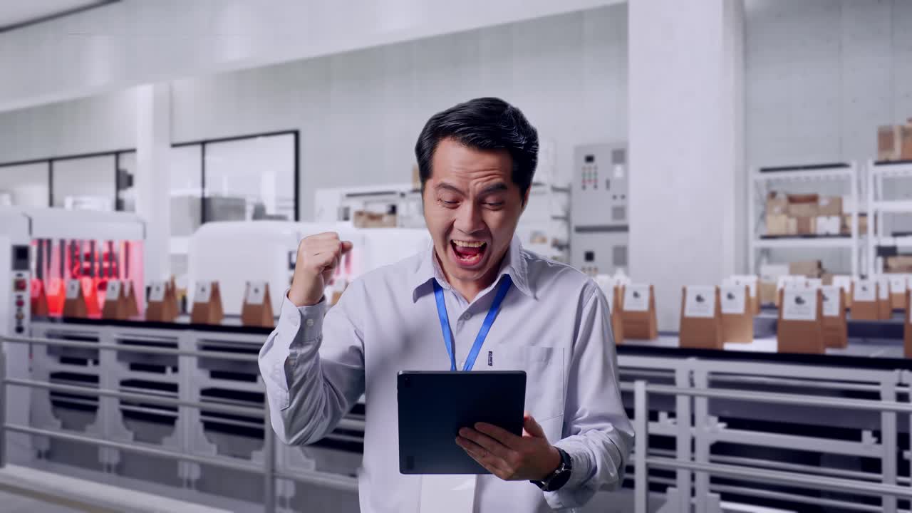 Asian Male Professional Worker Standing With His Tablet With Conveyor for Packaging Coffee Beans in Bags at Coffee Factory, He Raises His Fist Up With Screaming Goal