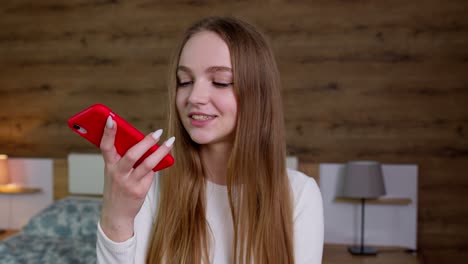 smiling young woman recording voice audio message to friends, using translator on mobile phone