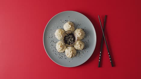 composition of plate with dim sum dumplings and chopsticks with soy sauce on red background