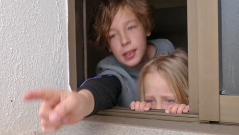 hermana y hermano mirando afuera a través de la ventana abierta de la casa