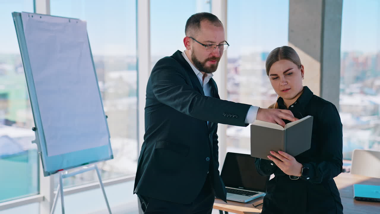 Businessman and secretary in office. Young woman with notebook talking with her boss in the light office with panoramic windows view on the city.