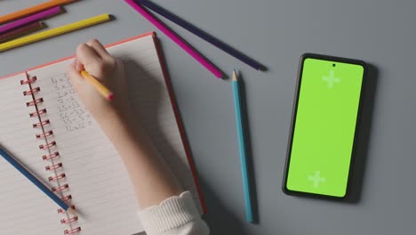 overhead shot of child with green screen mobile phone doing school maths homework in book