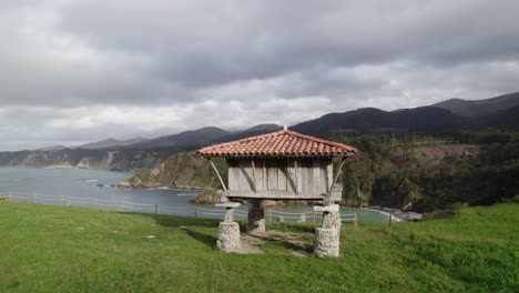 Backwards-dolly-shot-from-a-horreo-by-the-sea,-typical-granary-from-Asturias-the-north-of-the-Iberian-Peninsula,-traditional-farm-building