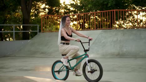 lovely young woman riding bmx bike in the sunlight outdoor skatepark. active people. pretty girl with dreadlocks freely riding