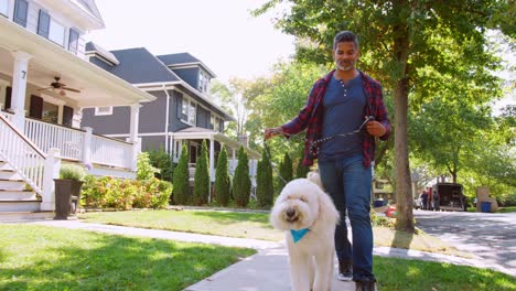 Low-Angle-Shot-Of-Man-Walking-Dog-Along-Suburban-Street